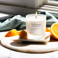 Candle labeled 'Lemongrass + Tangerine' on a marble surface with orange slices.