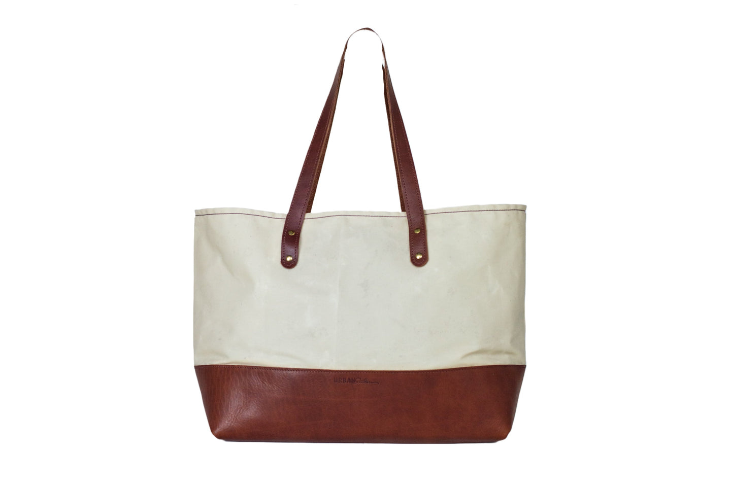 A canvas tote bag with brown leather bottom and straps stands against a white background.
