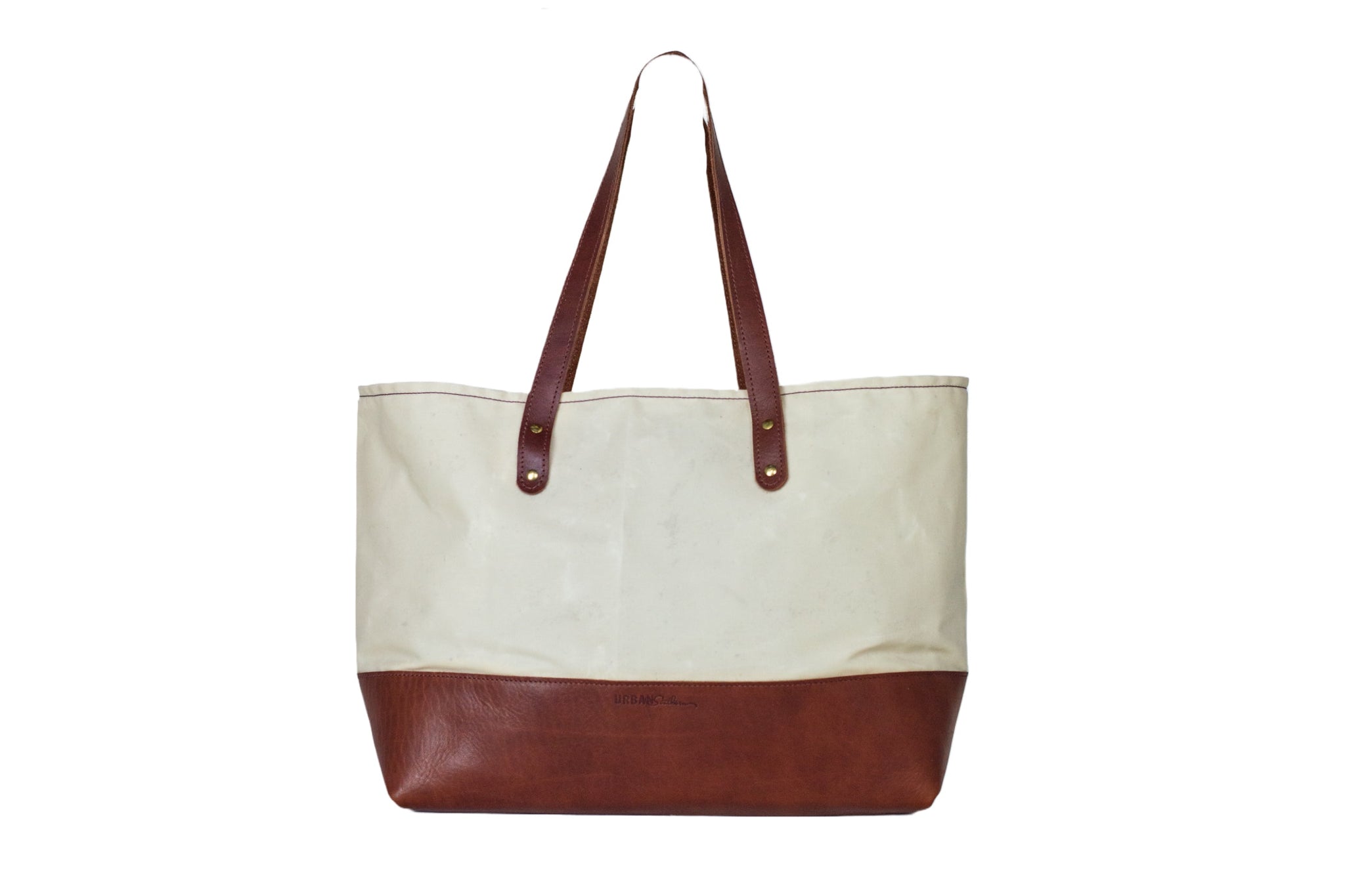A canvas tote bag with brown leather bottom and straps stands against a white background.
