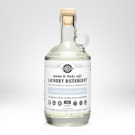 Rustic Strength presents their mama and baby safe, unscented laundry detergent in a clear glass jug with a wooden stopper.
