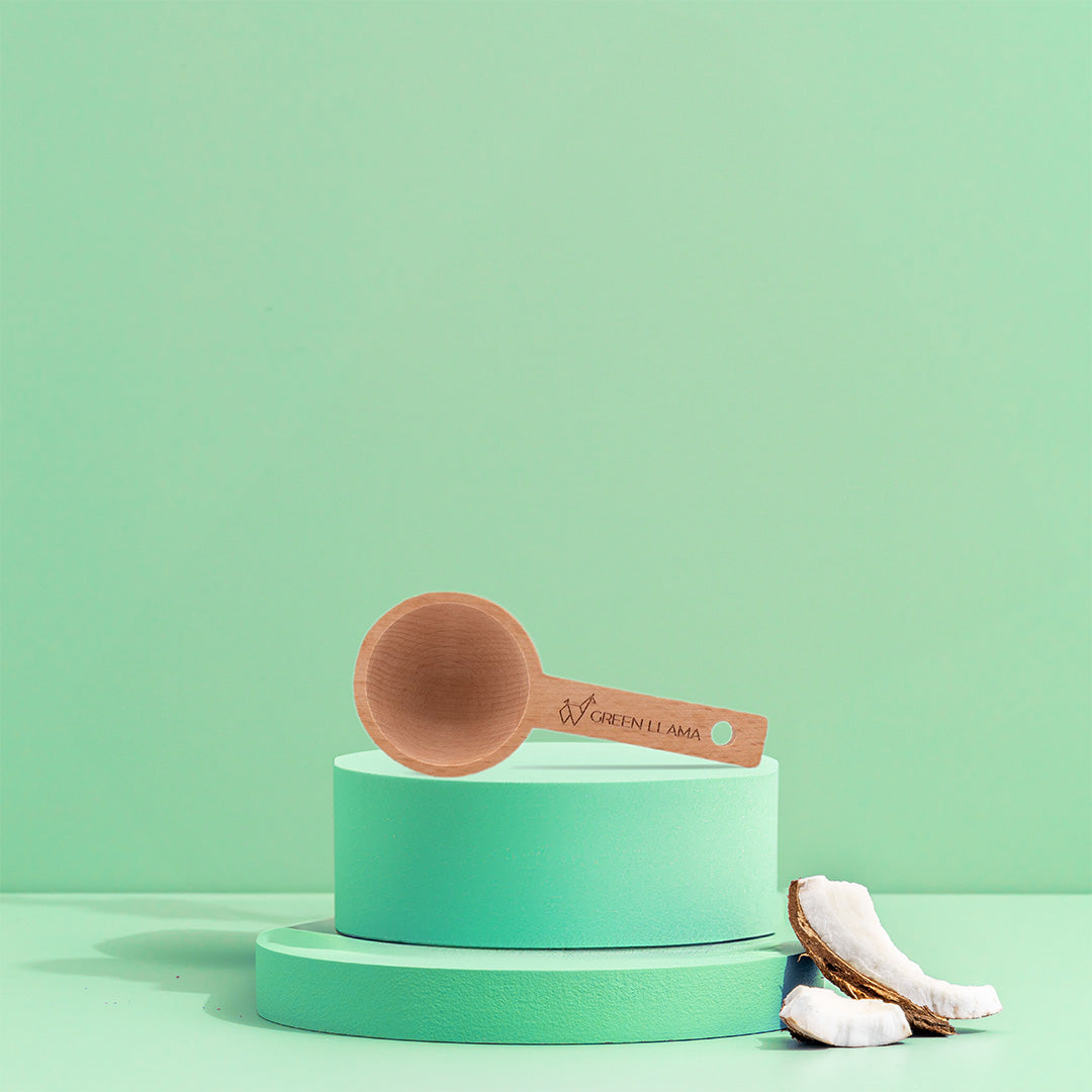 Green Llama wooden scoop sits on a turquoise pedestal beside coconut pieces.
