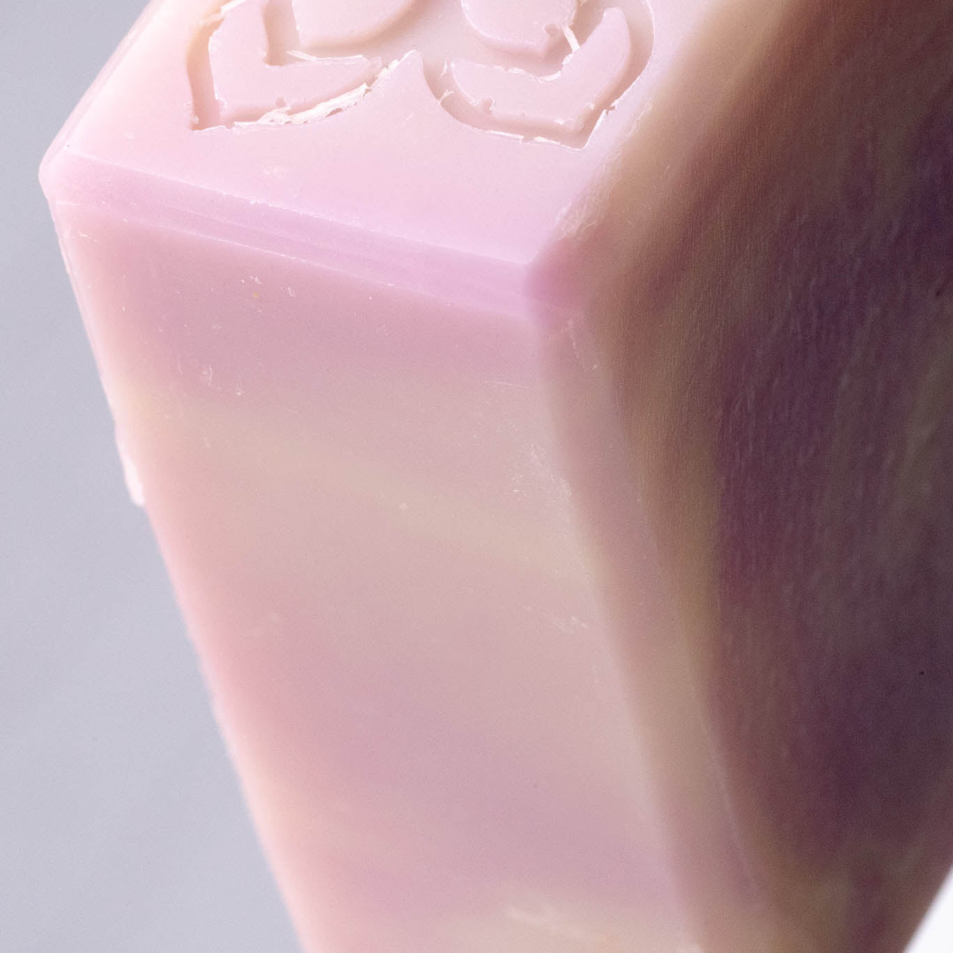 Close-up shows a pink and white bar of handmade soap featuring a heart design.
