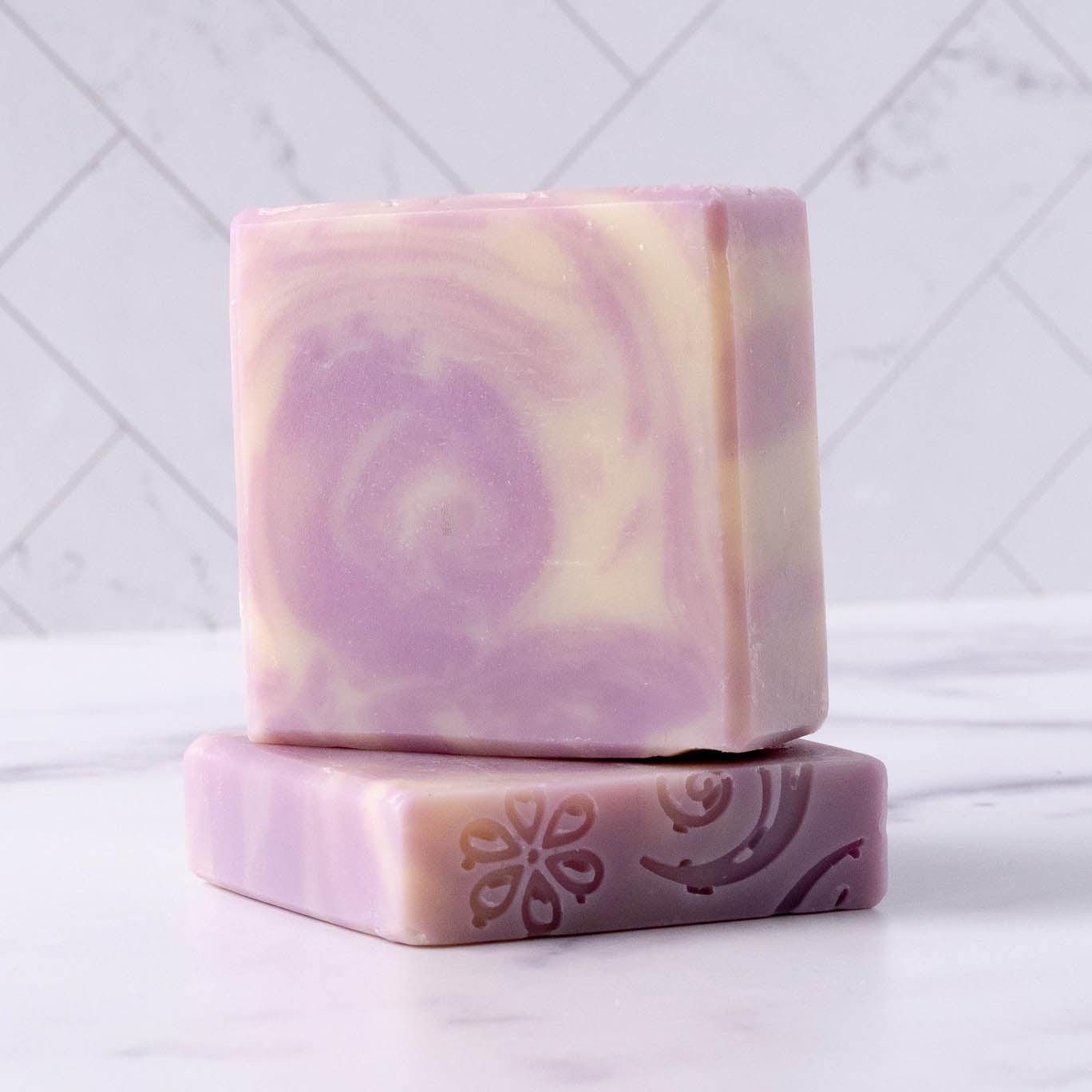 Handmade lavender soap bars display a floral design and swirling patterns.
