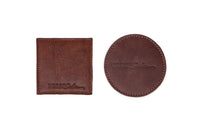 Two brown leather Urban Southern coasters, one square and one round, show stitched edges.
