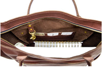 Open brown leather tote bag reveals a spiral notebook, card slots, and attached gold keychain.
