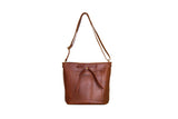 Displays a stylish brown leather crossbody bucket bag with adjustable strap and drawstring closure.
