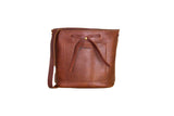 Showcases a stylish brown leather bucket bag with a drawstring closure and convenient front pocket.
