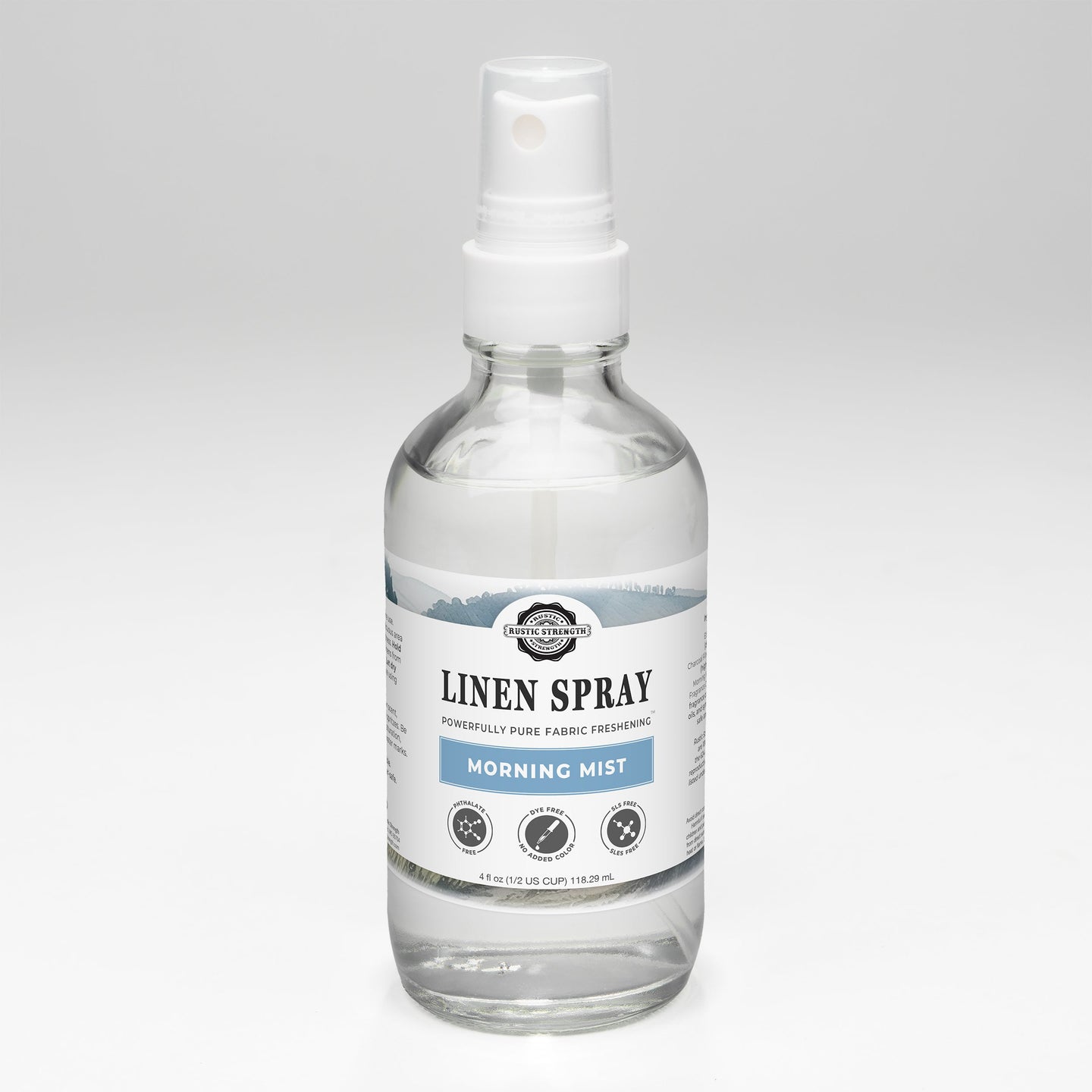 A clear bottle displays Rustic Strength Linen Spray in Morning Mist scent, promising powerfully pure fabric freshening.