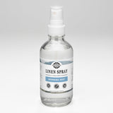 A clear bottle displays Rustic Strength Linen Spray in Morning Mist scent, promising powerfully pure fabric freshening.