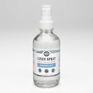 A clear bottle displays Rustic Strength Linen Spray in Morning Mist scent, promising powerfully pure fabric freshening.