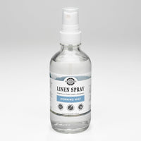 A clear bottle displays Rustic Strength Linen Spray in Morning Mist scent, promising powerfully pure fabric freshening.