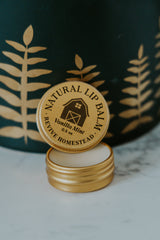 Revive Homestead markets their natural Vanilla Mint lip balm in a gold tin with a barn logo.
