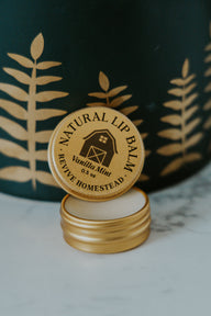 Revive Homestead markets their natural Vanilla Mint lip balm in a gold tin with a barn logo.
