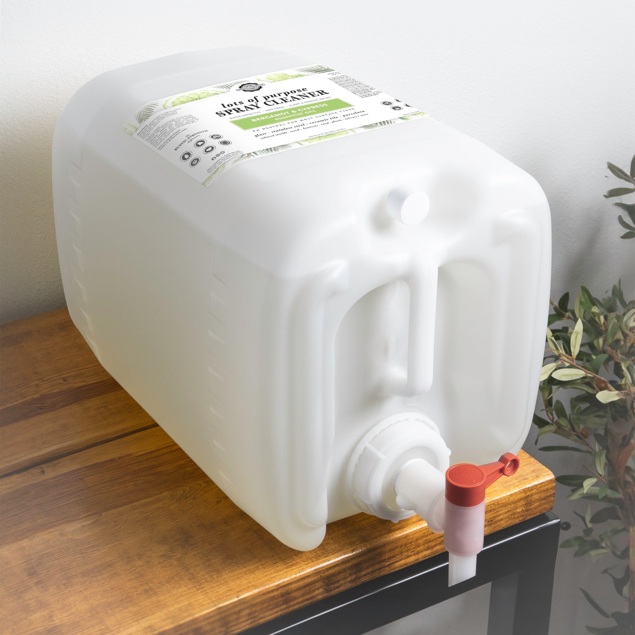 A large container of "Lots of Purpose" bergamot and cypress spray cleaner sits on a wooden table.