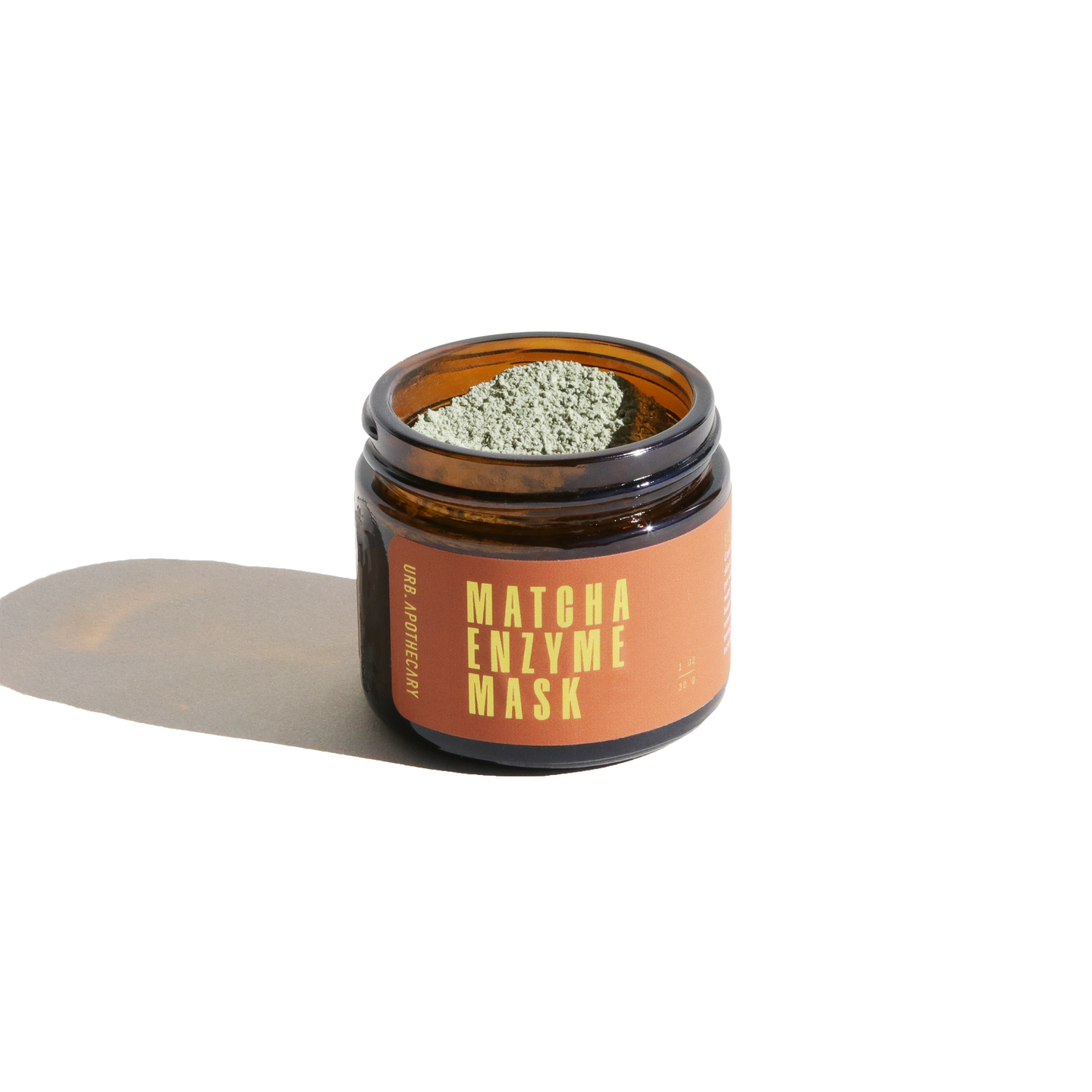 A full jar of Urb. Apothecary Matcha Enzyme Mask sits on a white surface, casting a shadow.
