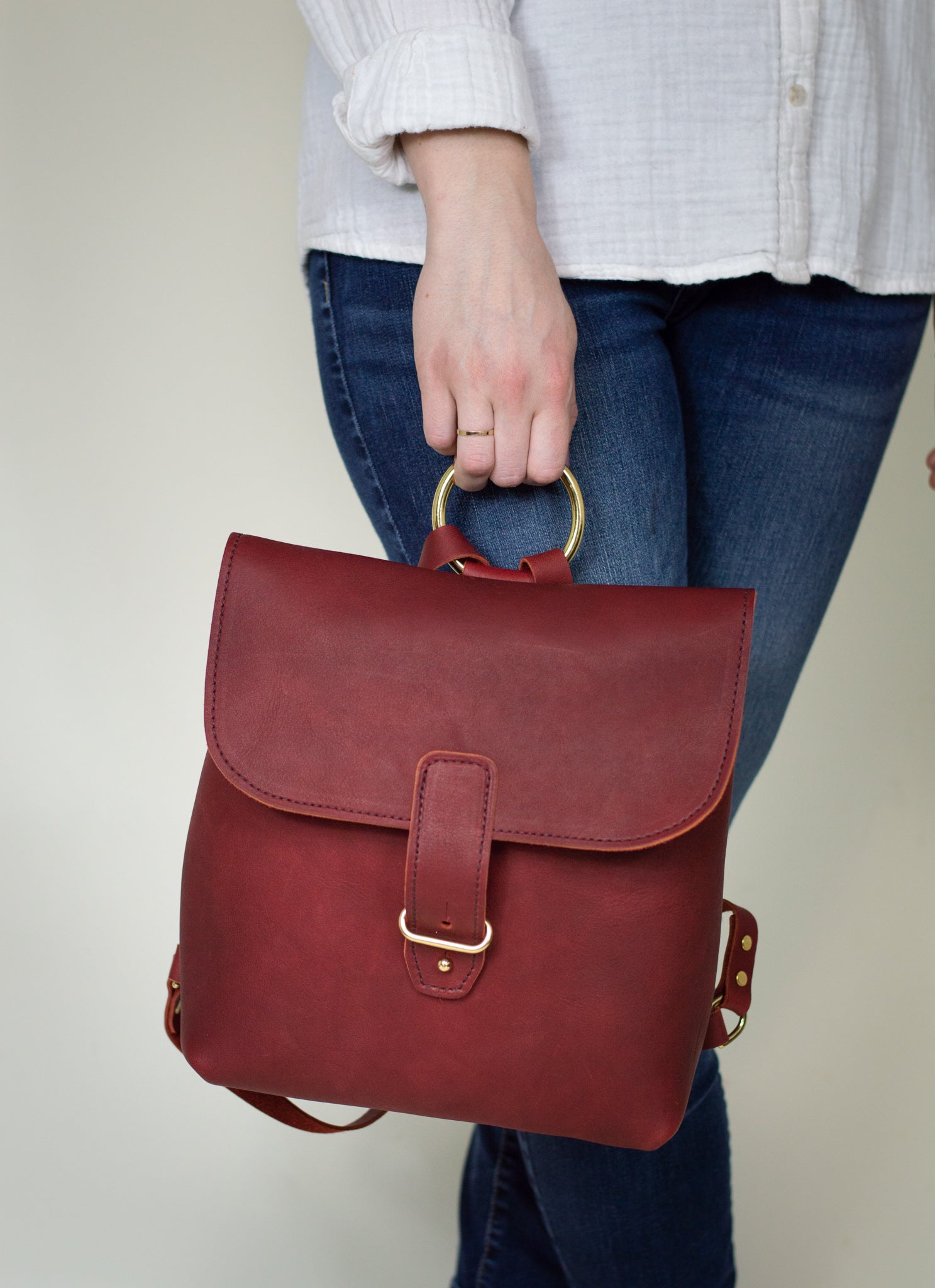 Person carries a stylish, handmade burgundy leather backpack with brass details.
