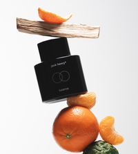 Jack Henry Balance cologne bottle balances precariously on citrus fruit and wood.
