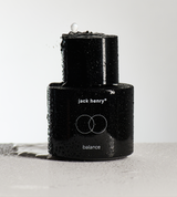 Water splashes onto a black Jack Henry Balance skincare product bottle.
