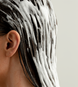 Close-up shows a woman washing her dark hair with foamy shampoo.

