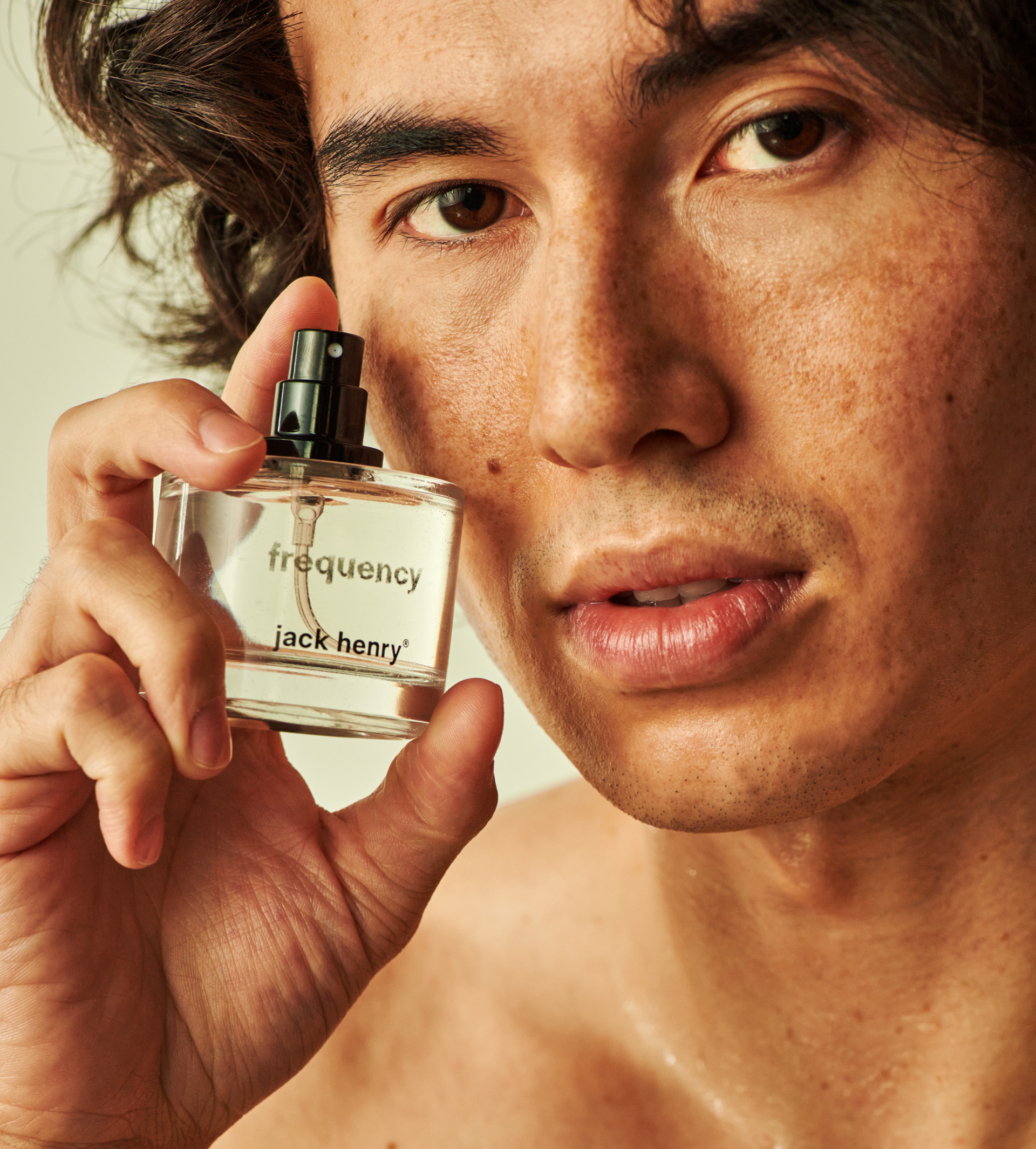 A man showcases Jack Henry Frequency fragrance, holding the clear bottle up close.
