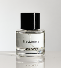 Jack Henry Frequency cologne bottle sits on a reflective surface.

