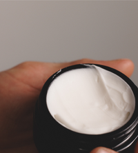 Hand holds a jar of luxurious, creamy white face moisturizer.
