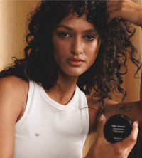 A woman with curly hair poses while holding Jack Henry hair cream.
