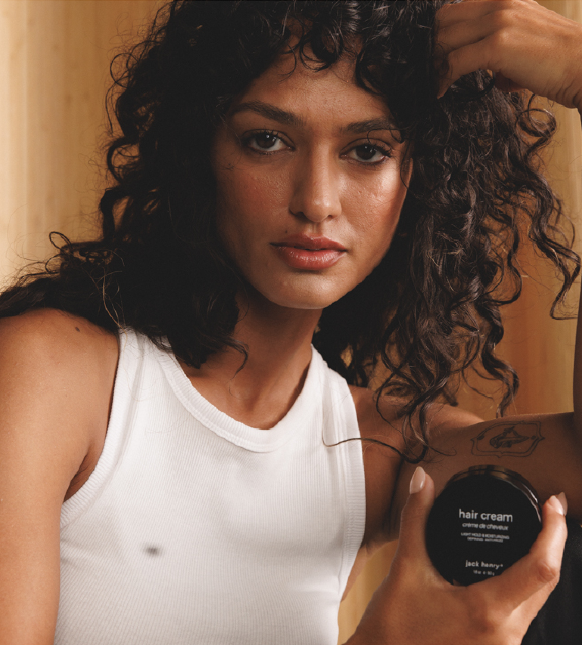A woman with curly hair poses while holding Jack Henry hair cream.
