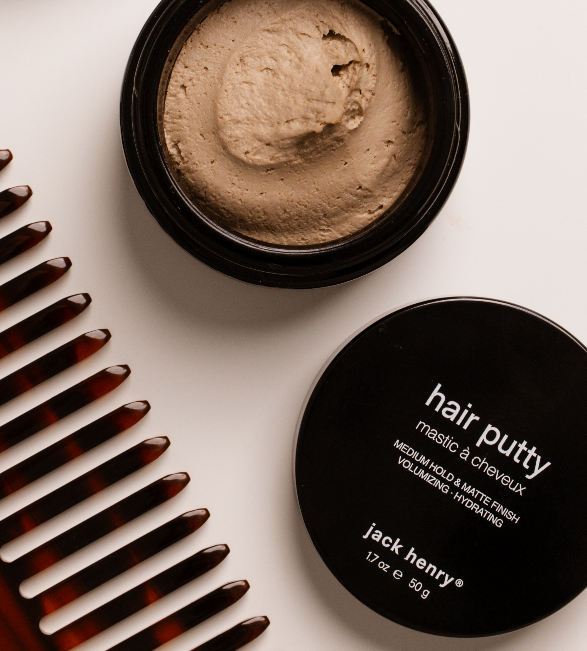 Stylists use Jack Henry Hair Putty from the opened jar for a medium hold and matte finish, while a tortoiseshell comb sits beside the product.
