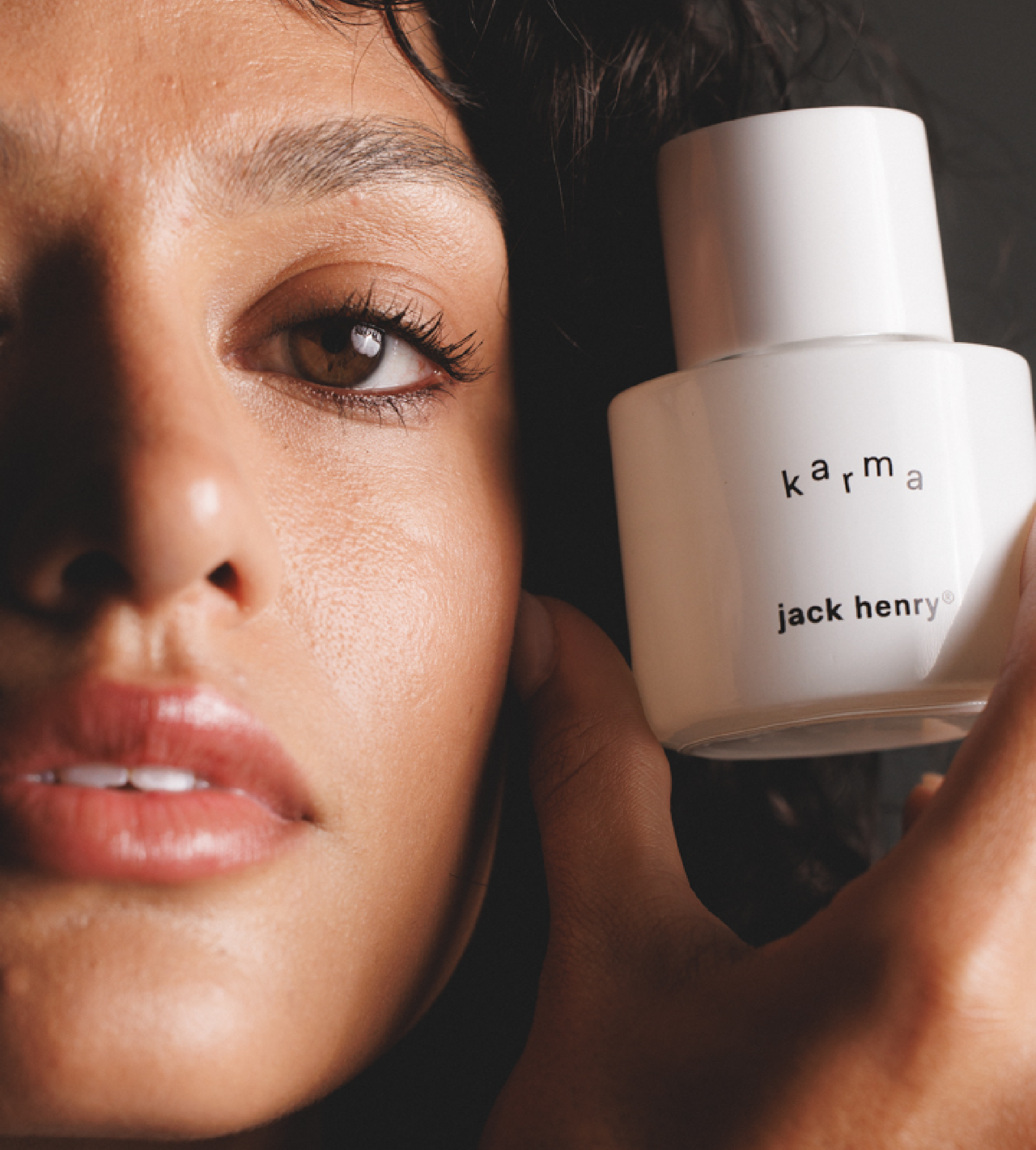 A woman's face partially appears beside a bottle of Jack Henry Karma face serum.

