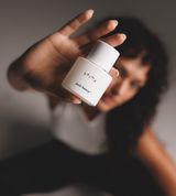 A woman presents a white "Karma" by Jack Henry® fragrance bottle toward the viewer.
