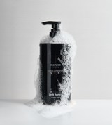 Jack Henry shampoo bottle overflows with cleansing bubbles on a glossy white surface.
