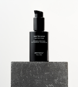 Jack Henry's black bottle of anti-aging Super Face Serum sits on a textured gray stone block.
