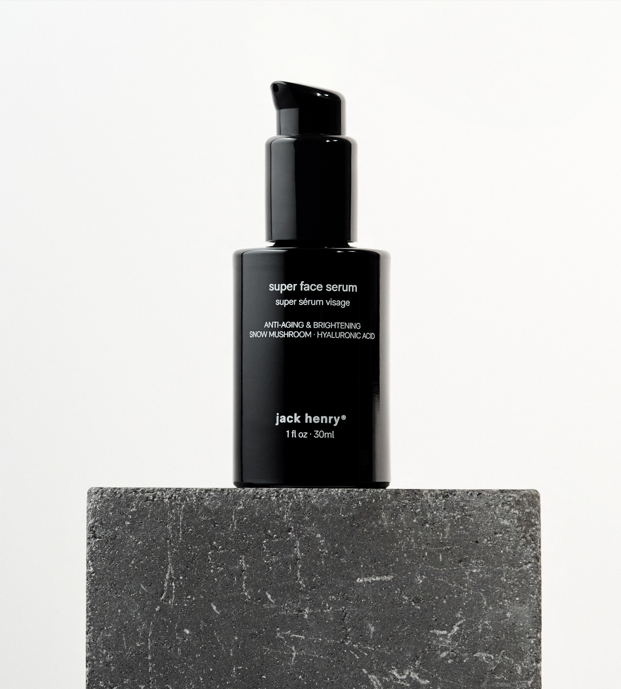 Jack Henry's black bottle of anti-aging Super Face Serum sits on a textured gray stone block.
