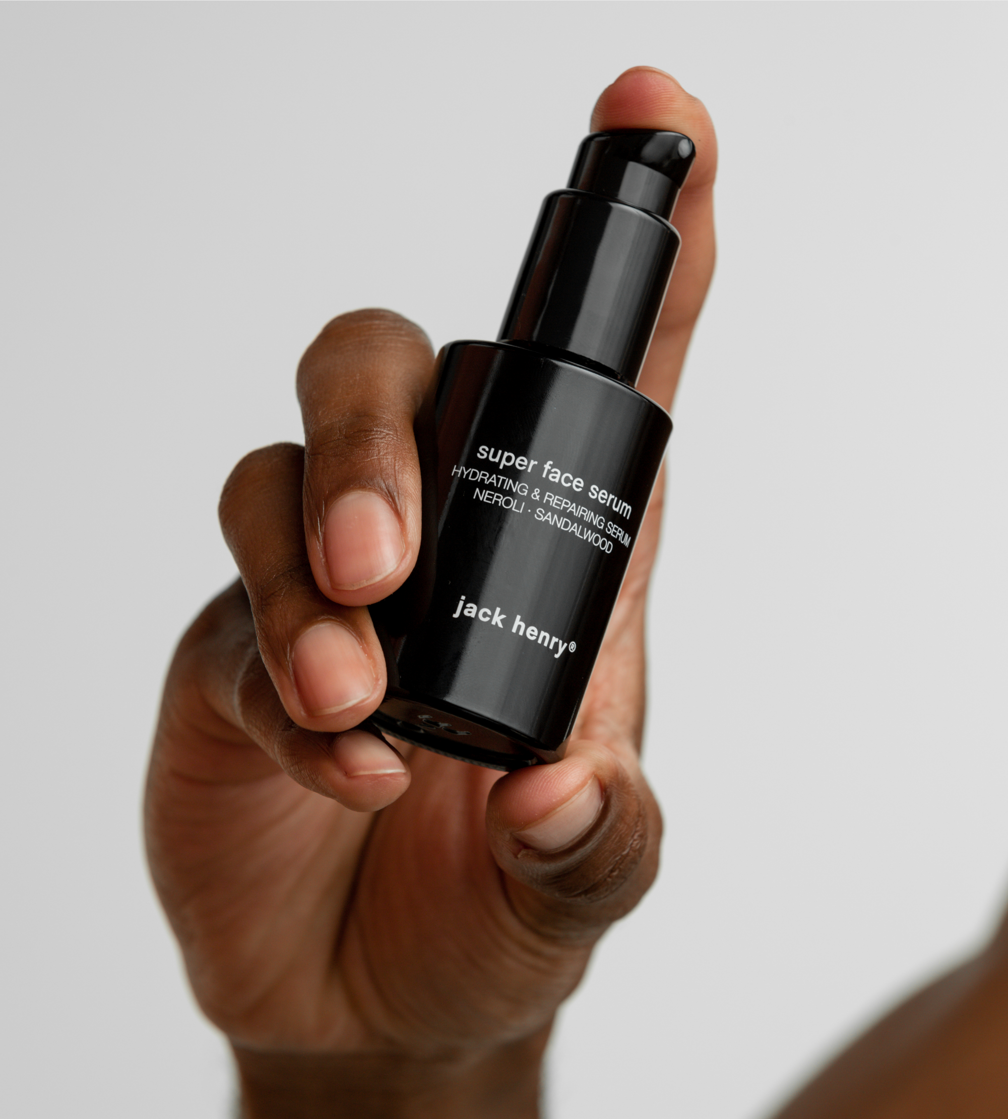 A hand holds a black bottle of Jack Henry Super Face Serum.
