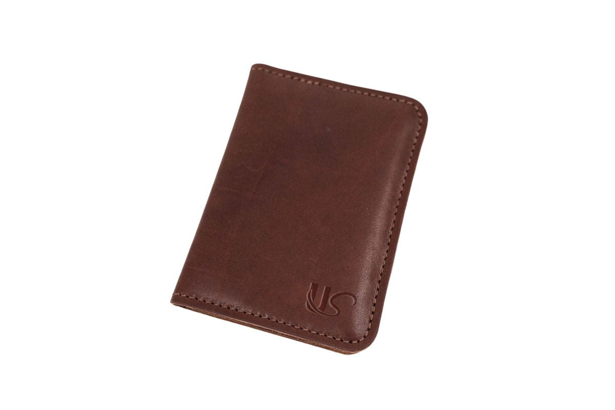 A brown leather card holder displays a minimalist design and subtle logo on a white background.
