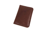 A brown leather card holder displays a minimalist design and subtle logo on a white background.
