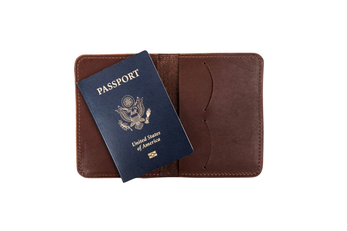 Shows a blue United States passport resting on an open, brown leather passport holder.
