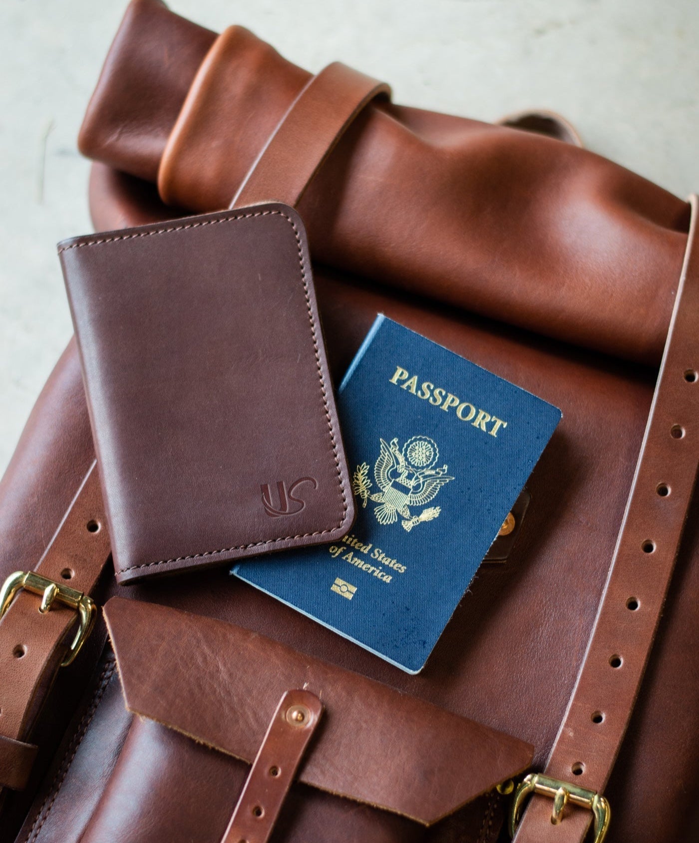 A brown leather travel backpack displays a passport and a matching passport wallet, suggesting international travel.
