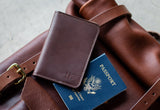 A brown leather passport wallet and a US passport sit atop a leather travel bag.
