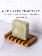 A marbled green soap bar sits on a teak wood tray, promoting a free teak tray offer with purchase of two 5oz bar soaps.
