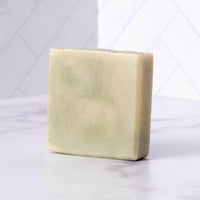 Artisan soap bar rests on a marble surface against a geometric white tile background.
