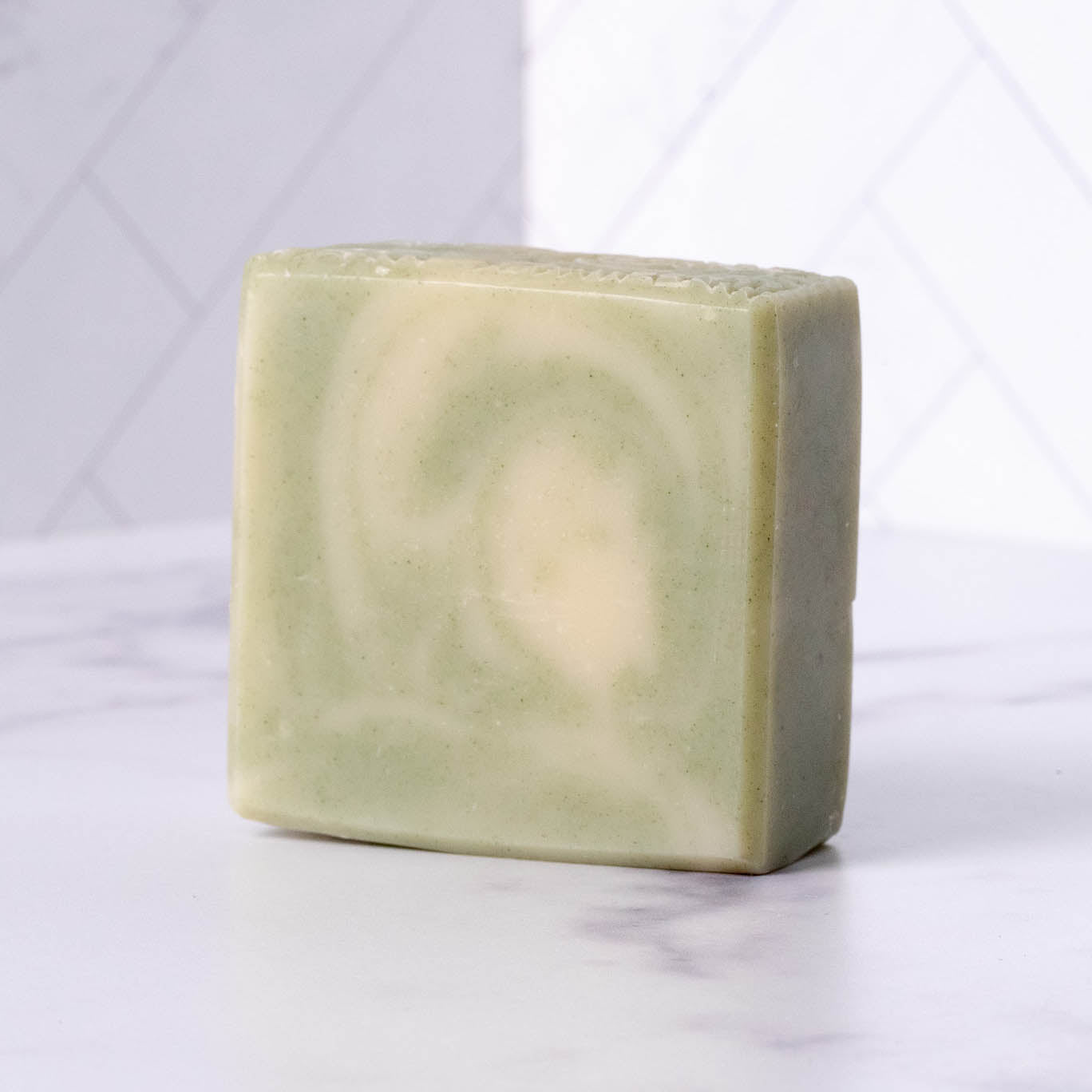A bar of swirl-patterned, natural handmade soap sits on a white marble countertop.
