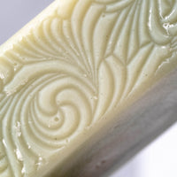 Close-up reveals the carved floral design on a pale green bar of handmade soap.
