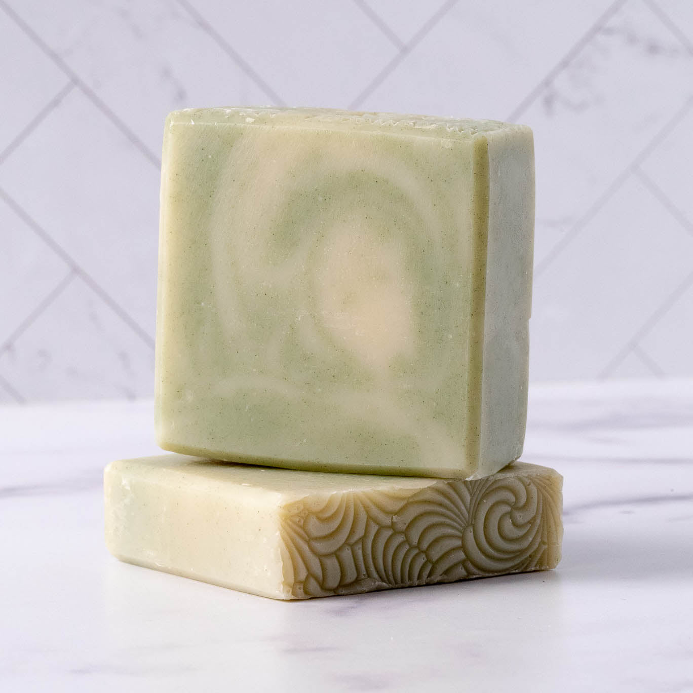 Two bars of natural, handcrafted soap rest stacked on a marble surface, displaying their unique patterns and textures.
