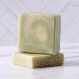 Two bars of natural, handcrafted soap rest stacked on a marble surface, displaying their unique patterns and textures.
