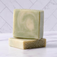 Two bars of natural, handcrafted soap rest stacked on a marble surface, displaying their unique patterns and textures.
