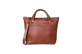 Showcases a stylish brown leather tote bag with shoulder strap and front pocket, against a white background.
