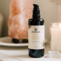 Annmarie Radiant Skin Silk lotion sits near a lit candle and Himalayan salt lamp.
