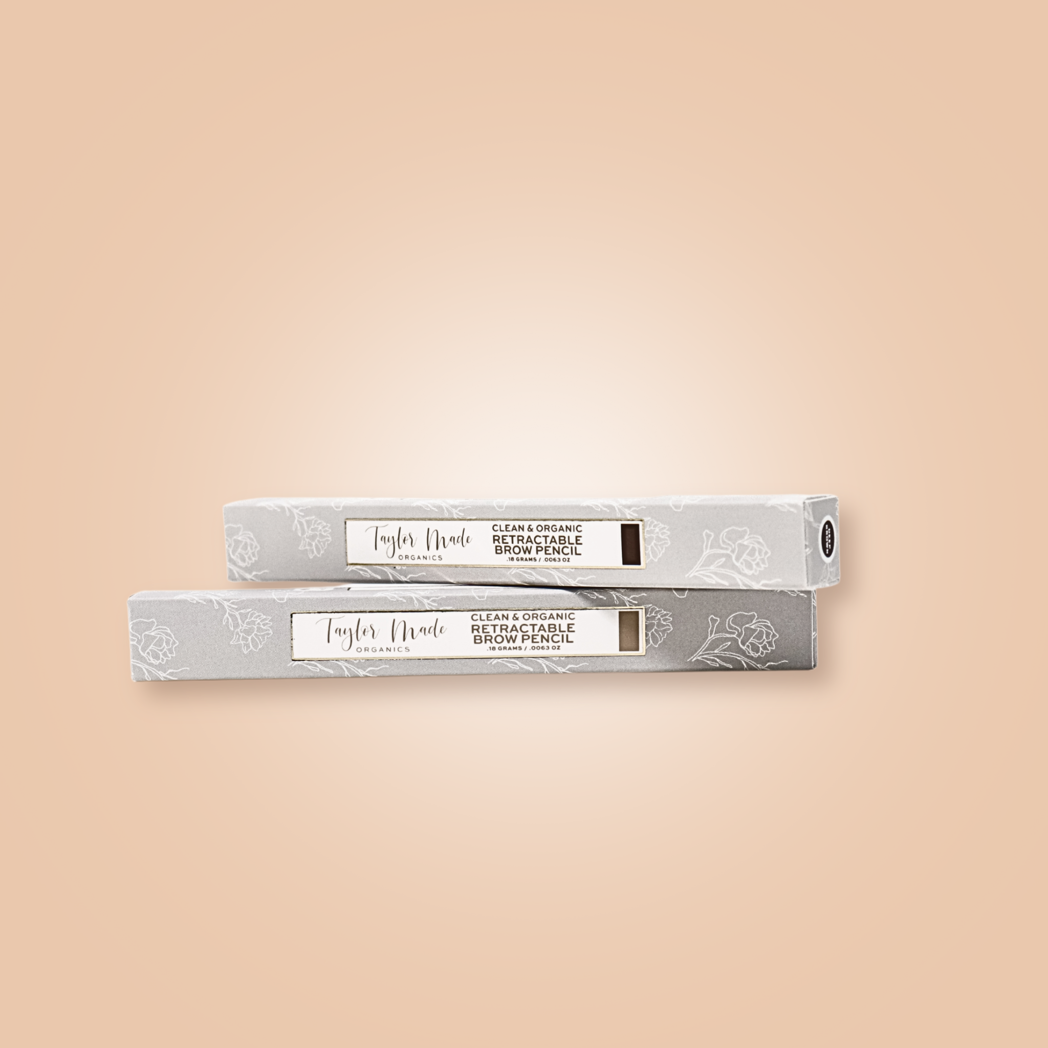 Two boxes of Taylor Made Organics retractable brow pencils sit stacked on a peach background.
